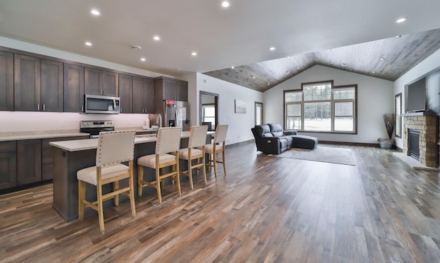 kitchen featuring a breakfast bar, a kitchen island with sink, stainless steel appliances, light stone countertops, and dark hardwood / wood-style flooring