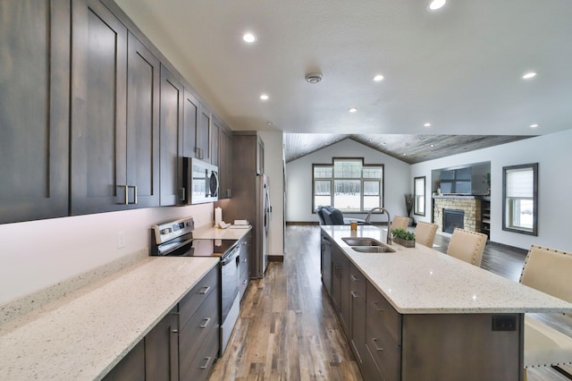 kitchen featuring appliances with stainless steel finishes, a breakfast bar, an island with sink, sink, and light stone countertops