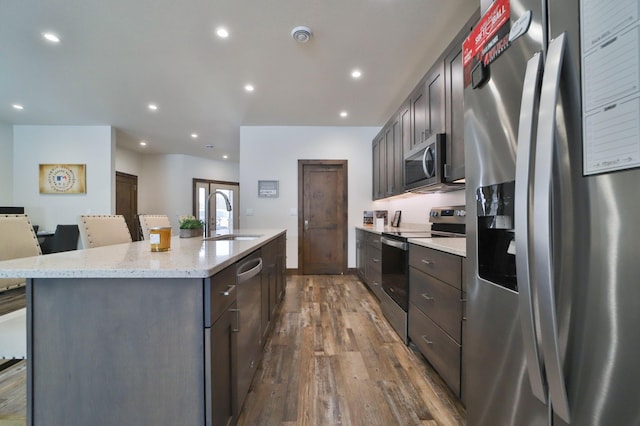 kitchen featuring a breakfast bar, wood-type flooring, sink, stainless steel appliances, and a center island with sink