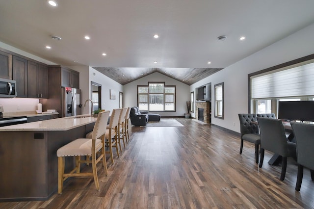 kitchen with lofted ceiling, a breakfast bar area, dark brown cabinets, an island with sink, and stainless steel appliances