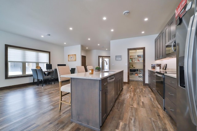 kitchen featuring sink, dark hardwood / wood-style flooring, stainless steel appliances, dark brown cabinets, and a center island with sink