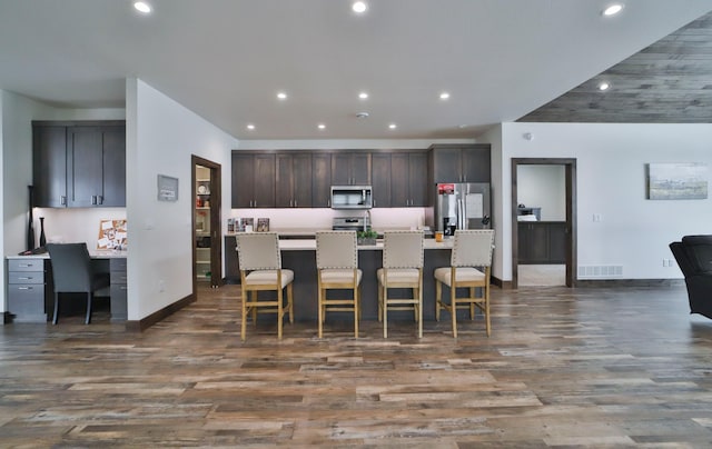 kitchen featuring a breakfast bar area, built in desk, dark brown cabinets, appliances with stainless steel finishes, and a kitchen island with sink