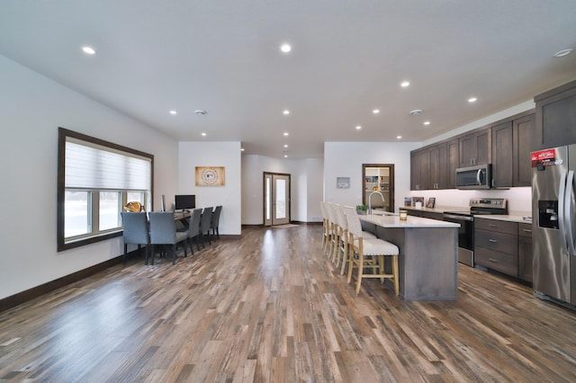 kitchen featuring a breakfast bar area, dark hardwood / wood-style flooring, stainless steel appliances, dark brown cabinets, and a center island with sink