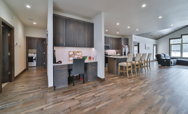 kitchen featuring dark hardwood / wood-style flooring, a kitchen bar, a kitchen island with sink, dark brown cabinetry, and stainless steel appliances