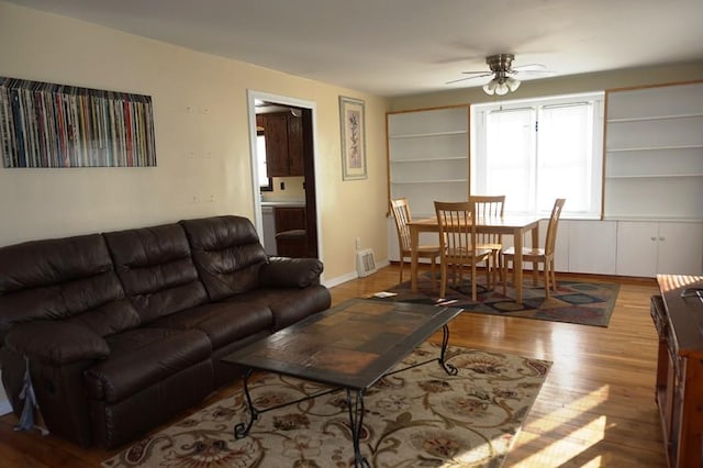 living room with built in shelves, ceiling fan, and light hardwood / wood-style flooring