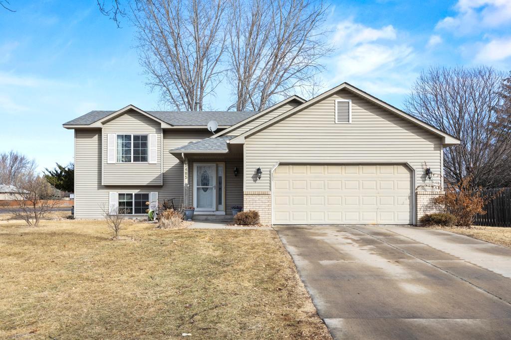 split level home featuring a shingled roof, concrete driveway, an attached garage, a front lawn, and brick siding