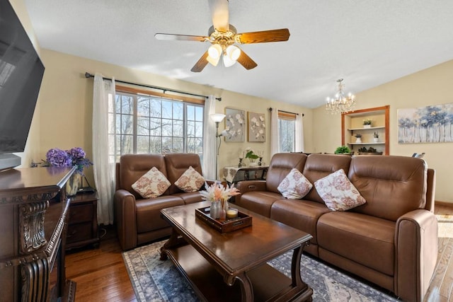 living area with lofted ceiling, a healthy amount of sunlight, hardwood / wood-style floors, and ceiling fan with notable chandelier