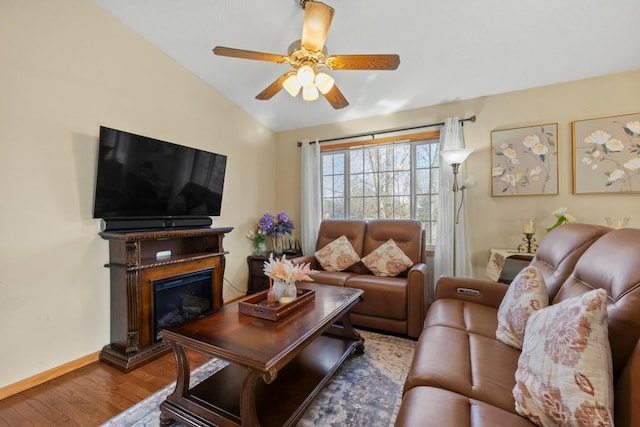 living area with a glass covered fireplace, ceiling fan, vaulted ceiling, wood finished floors, and baseboards