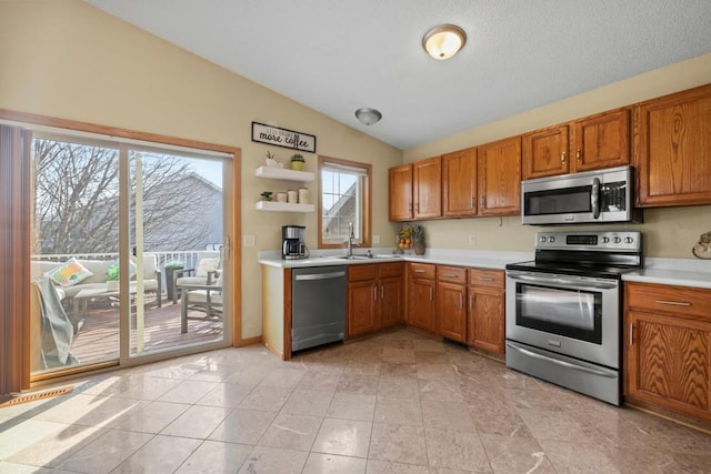 kitchen featuring lofted ceiling, a sink, light countertops, appliances with stainless steel finishes, and brown cabinets