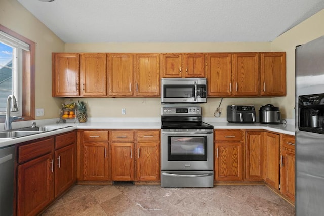 kitchen with appliances with stainless steel finishes, light countertops, brown cabinetry, and a sink