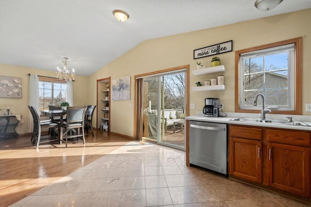 kitchen with dishwasher, brown cabinets, vaulted ceiling, light countertops, and a sink