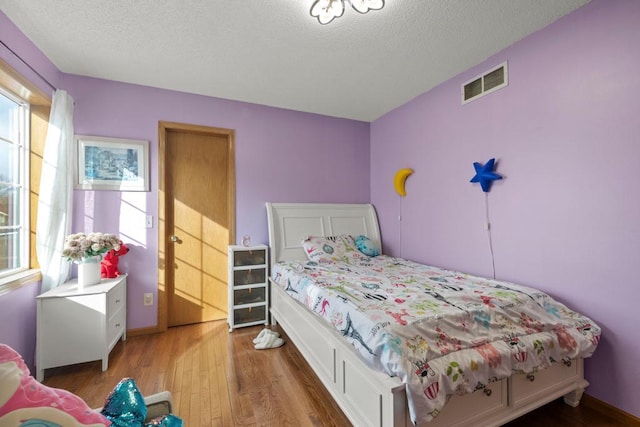 bedroom featuring light wood finished floors, baseboards, visible vents, and a textured ceiling