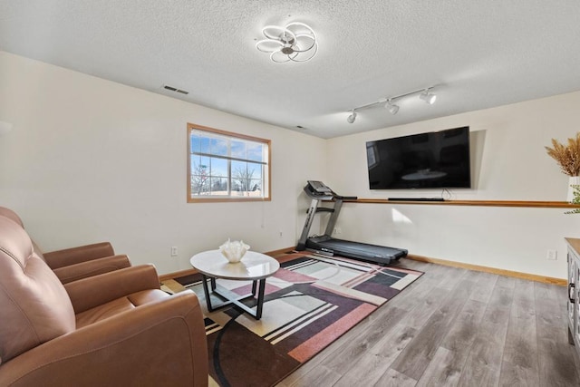 living area with visible vents, a textured ceiling, baseboards, and wood finished floors