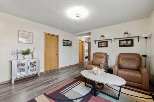 living area with a textured ceiling, baseboards, and wood finished floors