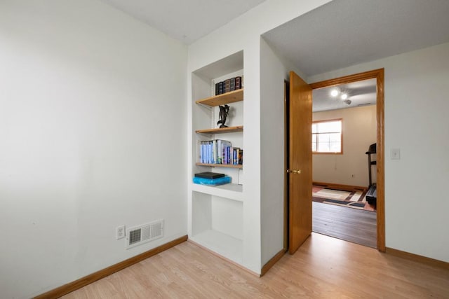 hallway featuring built in features, visible vents, light wood-style flooring, and baseboards