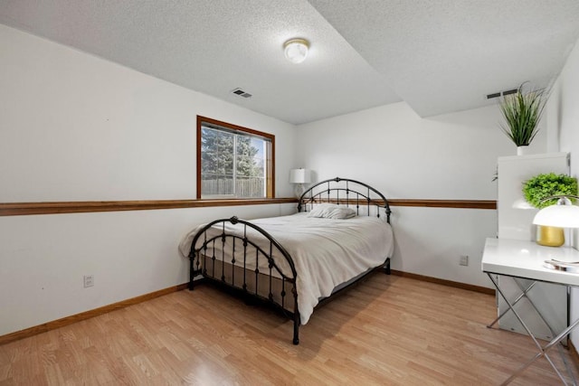 bedroom featuring light wood-style floors, visible vents, a textured ceiling, and baseboards