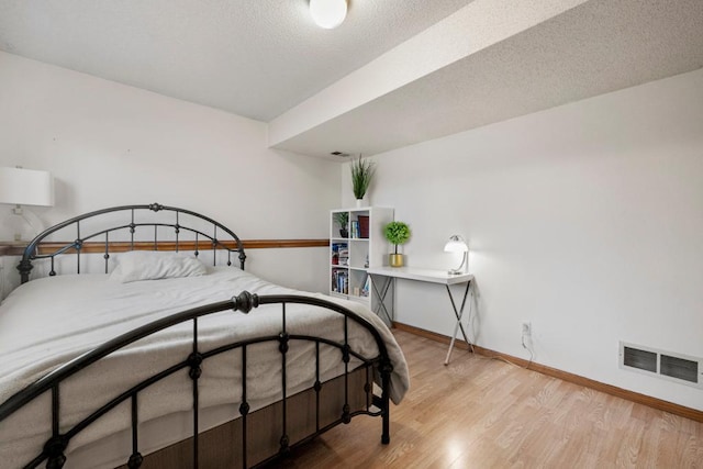 bedroom with a textured ceiling, wood finished floors, visible vents, and baseboards