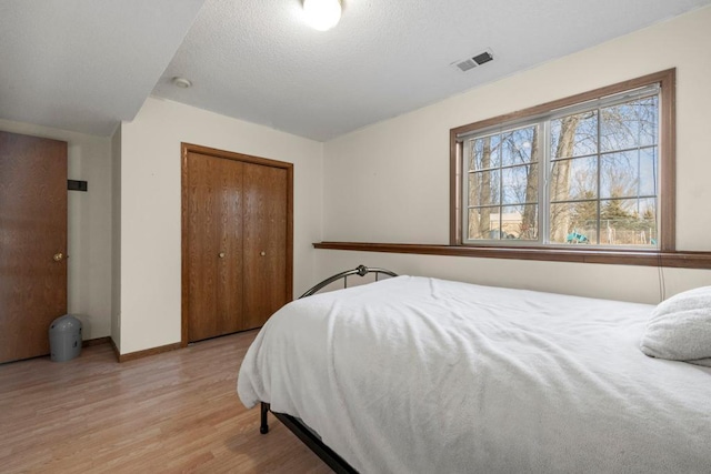 bedroom with a closet, visible vents, a textured ceiling, light wood-type flooring, and baseboards