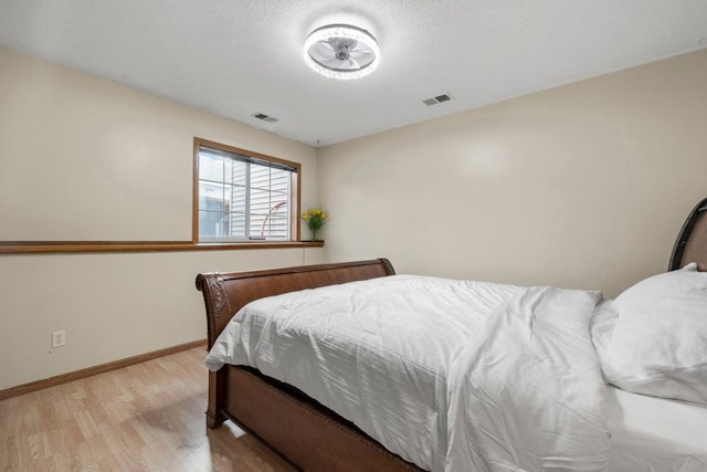 bedroom with light wood-style flooring, a textured ceiling, visible vents, and baseboards