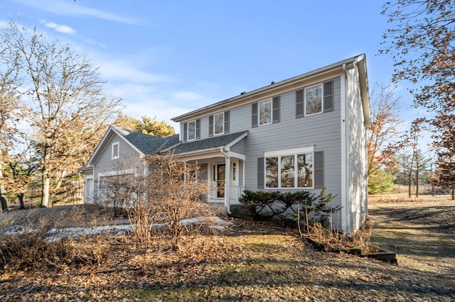 colonial inspired home with an attached garage, a shingled roof, and a porch