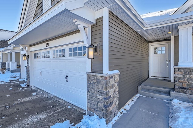 snow covered property entrance featuring a garage and stone siding