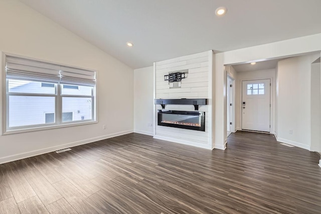 unfurnished living room featuring a glass covered fireplace, dark wood-style flooring, a healthy amount of sunlight, and vaulted ceiling