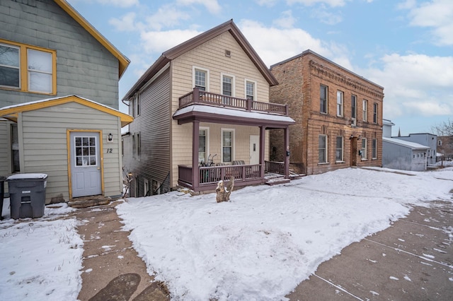 snow covered rear of property with a balcony and covered porch