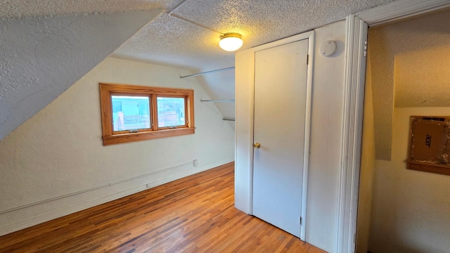 additional living space with vaulted ceiling, a textured ceiling, and light wood-type flooring