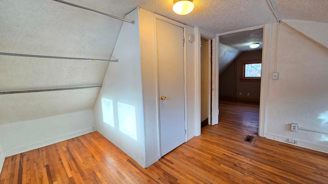 additional living space featuring wood-type flooring, a textured ceiling, and vaulted ceiling