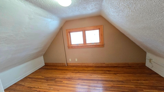 additional living space with lofted ceiling, hardwood / wood-style floors, and a textured ceiling