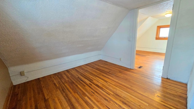 bonus room featuring lofted ceiling, visible vents, a textured ceiling, and wood finished floors