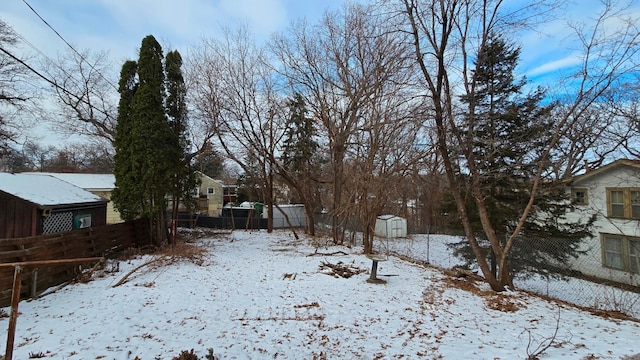 snowy yard with an outbuilding, fence, and a storage shed