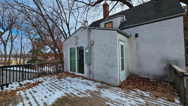 snow covered property with a chimney, a deck, and stucco siding