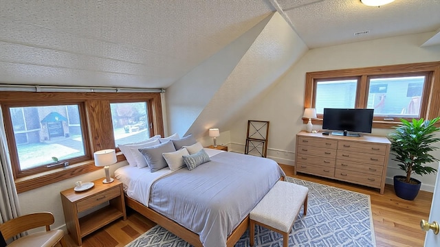 bedroom featuring a textured ceiling, light wood finished floors, lofted ceiling, and baseboards