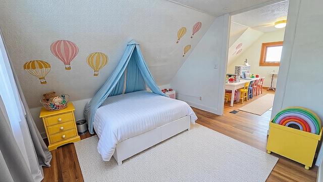 bedroom featuring lofted ceiling, a textured ceiling, baseboards, and wood finished floors