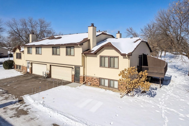 snow covered property with an attached garage and a chimney