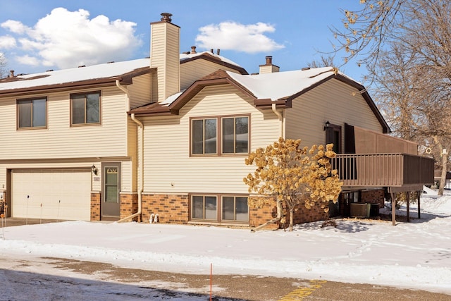 snow covered back of property featuring central AC, a chimney, and an attached garage