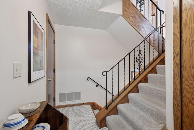 stairs with lofted ceiling, visible vents, and a textured ceiling