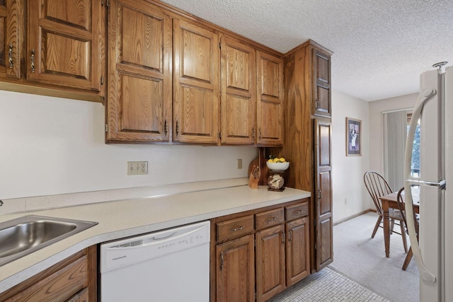 kitchen with brown cabinets, white appliances, light countertops, and a textured ceiling