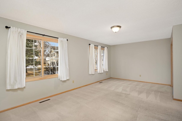 unfurnished room featuring baseboards, a wealth of natural light, visible vents, and light colored carpet