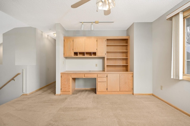 unfurnished office with baseboards, light colored carpet, built in desk, and a textured ceiling