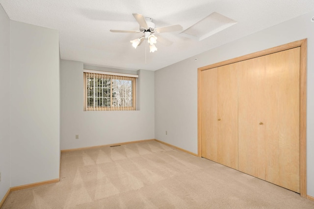 unfurnished bedroom featuring a closet, light colored carpet, a ceiling fan, a textured ceiling, and baseboards