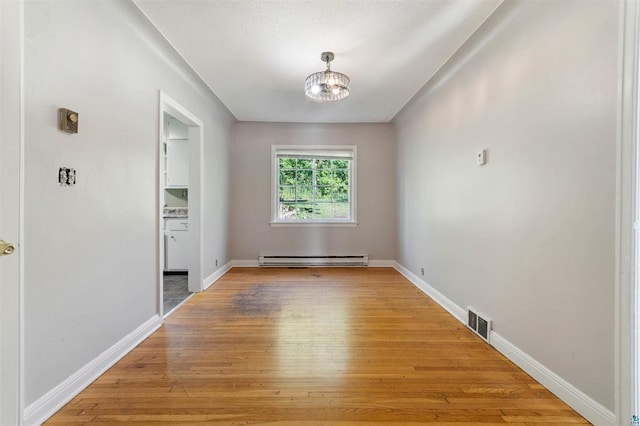 unfurnished room featuring an inviting chandelier, hardwood / wood-style floors, and baseboard heating