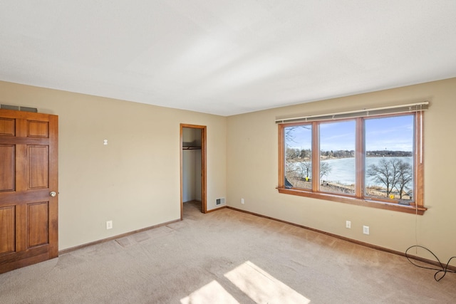 unfurnished bedroom with light carpet, visible vents, baseboards, a walk in closet, and a closet