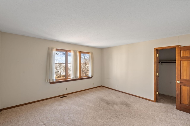 empty room with light colored carpet, visible vents, a textured ceiling, and baseboards