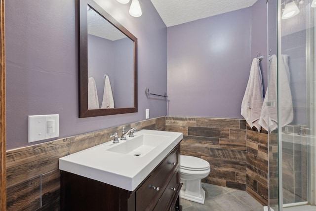 full bathroom with a textured ceiling, toilet, vanity, tile walls, and wainscoting