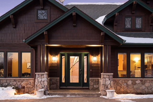 view of exterior entry with stone siding and a shingled roof