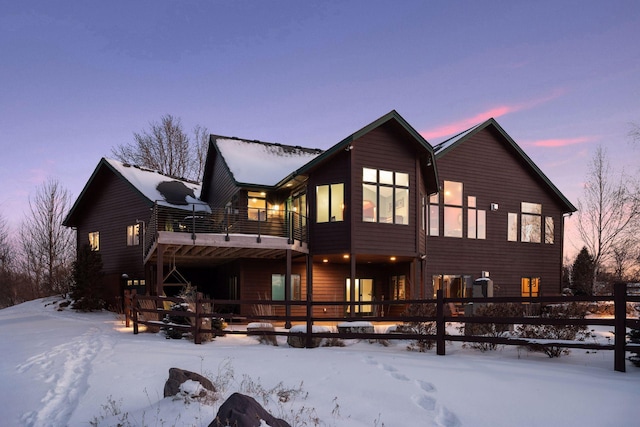 snow covered rear of property with a balcony and fence