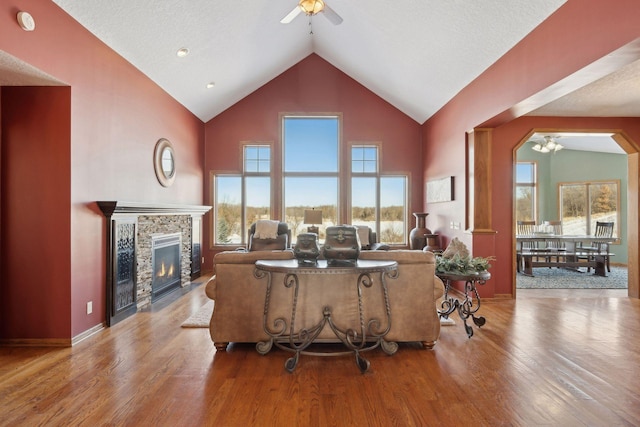 living area featuring high vaulted ceiling, a fireplace, light wood-style flooring, and ceiling fan