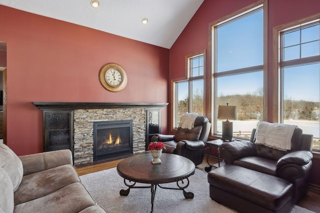 living room with plenty of natural light, high vaulted ceiling, wood finished floors, and a stone fireplace